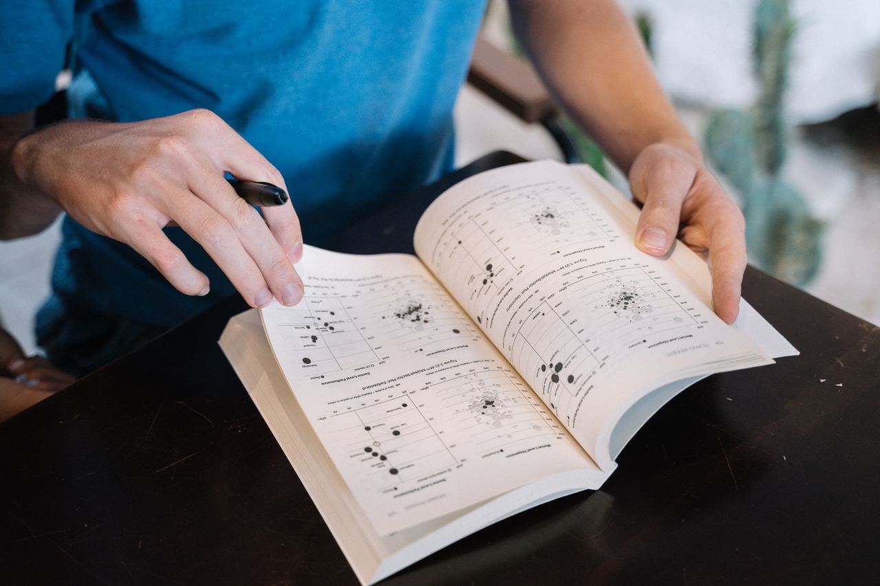Service Person flipping through a textbook, examining pages with scientific graphs. Ideal for educational contexts.