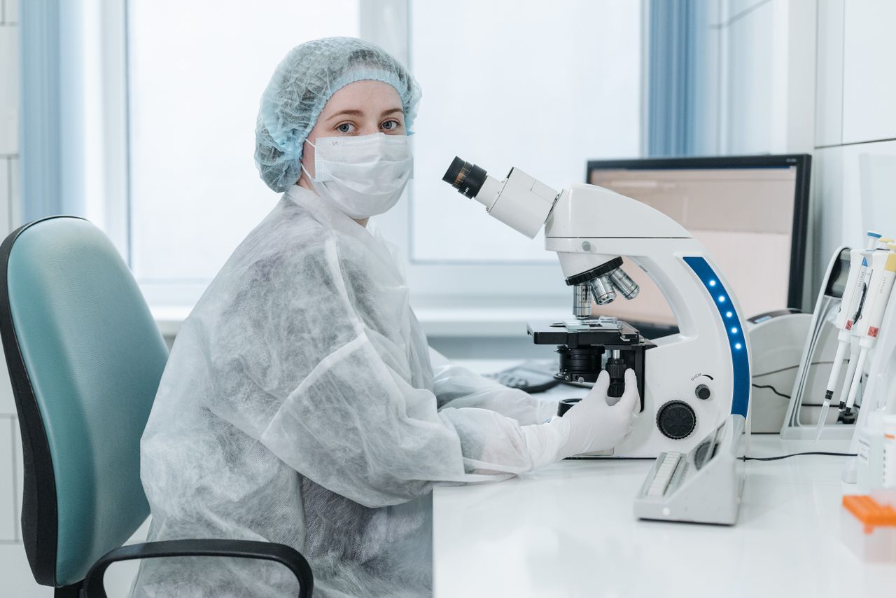 Service Woman lab technician examining samples with a trinocular microscope in a medical laboratory setting.